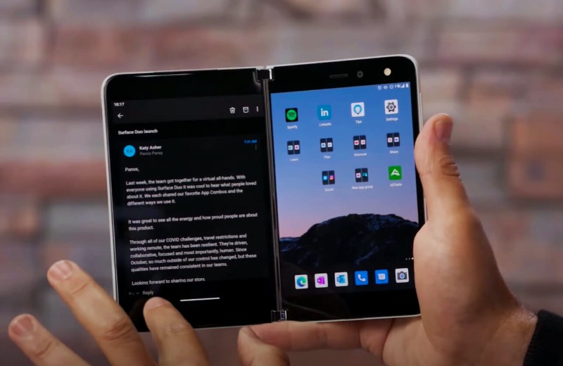 A dual-screen Surface Duo phone showing an email on the left screen and a grid of apps on the right screen