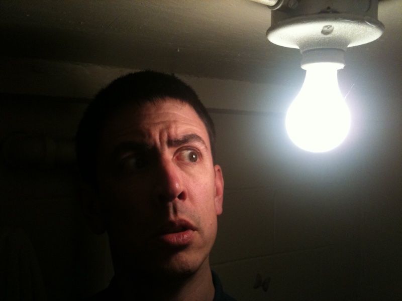 A tall man about to hit his head on a bare lightbulb in the ceiling