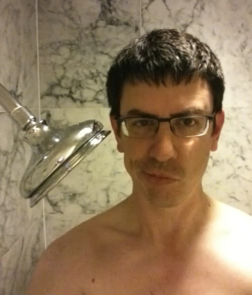 A disappointed tall man with a shower that only reaches as high as his shoulders